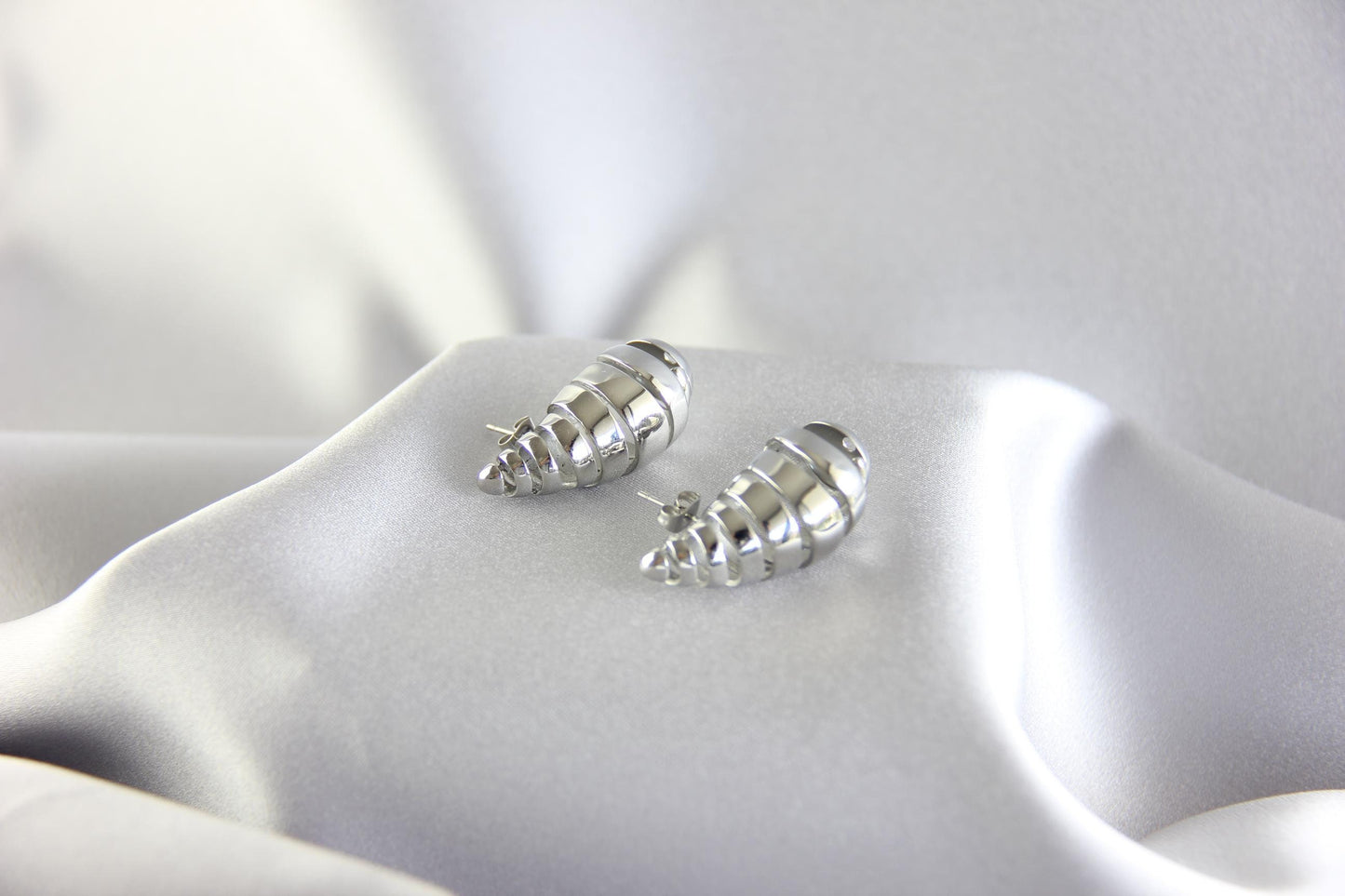 May include: A pair of silver shell-shaped earrings. The earrings are made of smooth, shiny metal and have a spiral design.